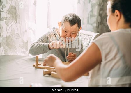 elderly woman with down syndrome and an Asian woman play in tower from wooden blocks Stock Photo