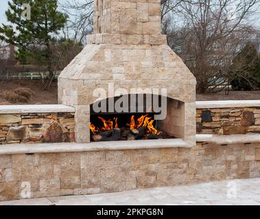 A gas fireplace made from paving stone burning outside on a patio close up. Stock Photo