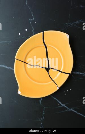 Top View of Vibrant Yellow Broken Ceramic Coaster on Black Marble Countertop Stock Photo
