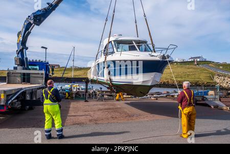 Lifting a small cabin cruiser from the water for repairs in the small harbour at Bridge End, West Burra, Shetland Isles, Scotland Stock Photo