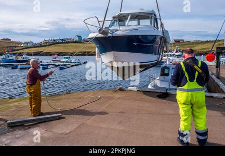 Lifting a small cabin cruiser from the water for repairs in the small harbour at Bridge End, West Burra, Shetland Isles, Scotland Stock Photo