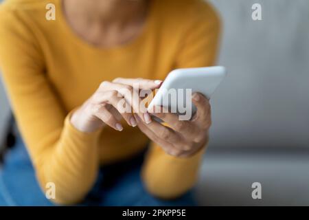 Unrecognizable Lady Using Modern Smartphone While Sitting On Couch At Home Stock Photo