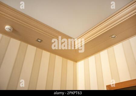Part of the living room, corner of the wall from the ceiling, mounted LED lights in a wooden console on the ceiling. Stock Photo