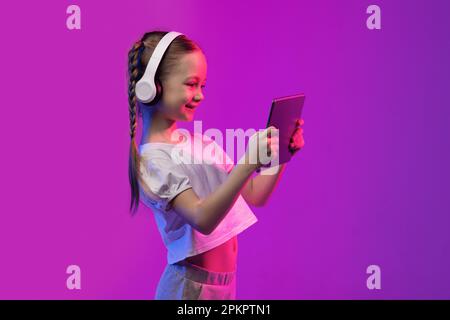 Happy school-age blonde girl using tablet and headphones, copy space Stock Photo