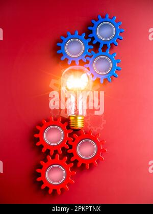 Shining light bulb connected between blue and red gear wheels on red background, vertical style. Business strategy, management and solution, human res Stock Photo