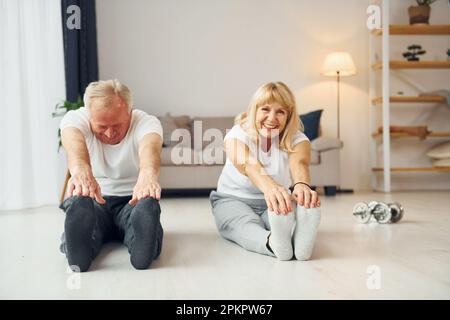 Sitting and doing exercises. Senior man and woman is together at home Stock Photo