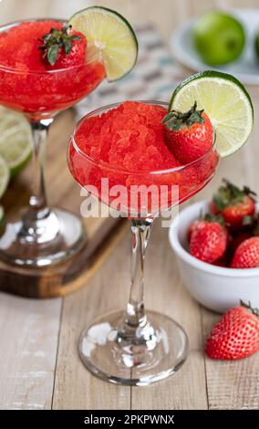 Frozen strawberry daiquiri garnished with strawberries and lime slice on a rustic wooden table Stock Photo