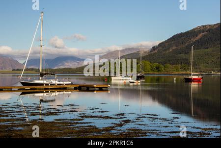 Sail boats on Loch Leven, reflecting in the Loch along with the surrounding cloud-capped mountains, in the Western Scottish Highlands Stock Photo