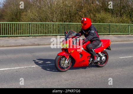 1999 90s nineties Red Honda Vfr800f V Four Motorcycle  Sports Tourer Petrol 781 cc with a rider wearing Red Mandeep Motorbike Helmet Cover Fluffy Funny plush full face helmets, crossing motorway bridge in Greater Manchester, UK Stock Photo