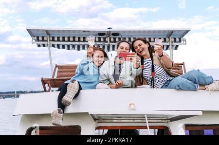 Three women friends have party on roof of tourboat, taking selfie and drinking wine. Stock Photo