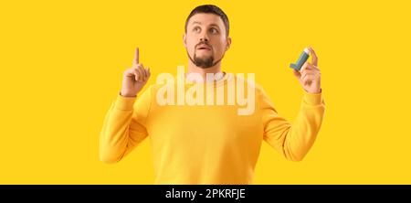 Man with inhaler and raised index finger on yellow background Stock Photo