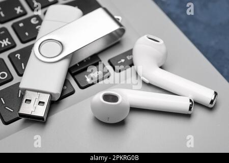 White USB flash drive and wireless earphones on modern laptop, closeup Stock Photo