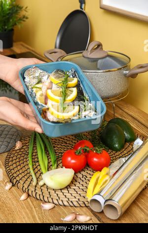 Woman holding baking dish with raw fish and vegetables in kitchen Stock Photo