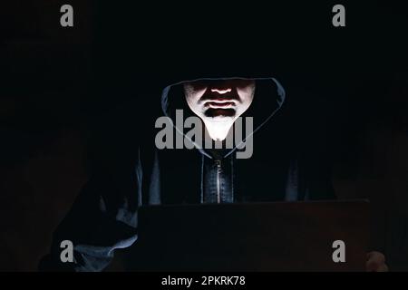 Man in the hoodie sitting in front of the laptop at night. Hacker, cyber criminal, stealing personal data Stock Photo
