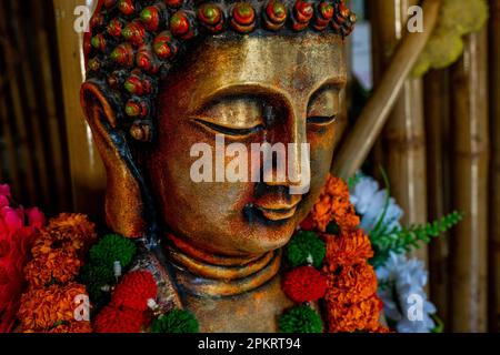 Close up of bronze buddha statue sitting in meditation with flower decorations for festival ceremony. High quality photo Stock Photo