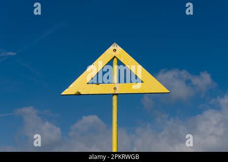 Triangular yellow arrow sign against a blue sky Stock Photo