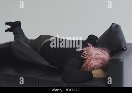 A drunken man in a pink wig climbs over the sofa and falls asleep. Stock Photo