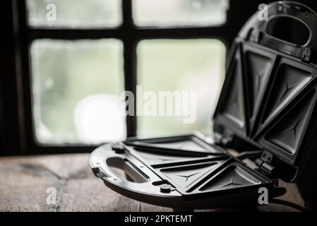 Open empty sandwich maker on the background of an old-fashioned house window. Stock Photo