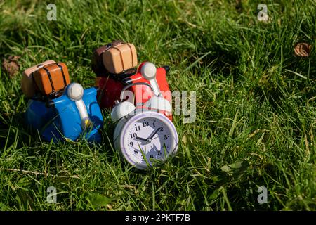 Toy scooters and alarm clock on green grass. Delivery, travel concept. Stock Photo