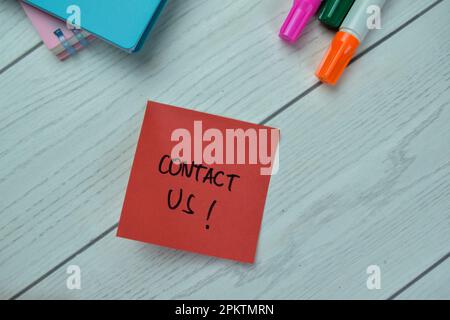 Concept of Contact Us! write on sticky notes isolated on Wooden Table. Stock Photo