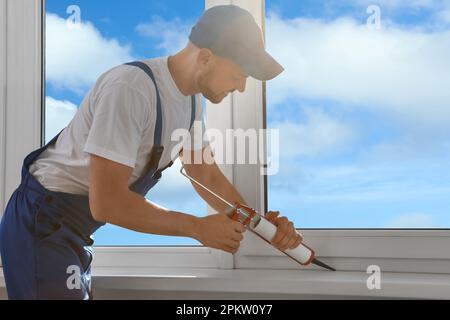 Worker sealing plastic window with caulk indoors. Installation process Stock Photo