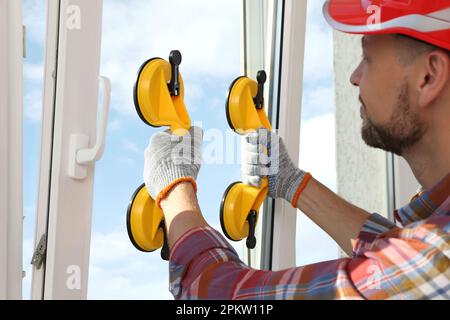 Worker using suction lifters during plastic window installation indoors Stock Photo