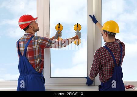 Workers using suction lifters during plastic window installation indoors Stock Photo