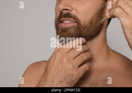 Man applying oil onto beard on grey background, closeup Stock Photo