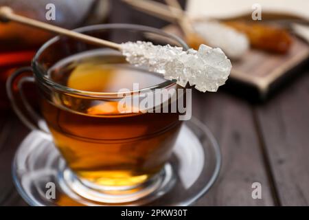 Stick with sugar crystals and cup of tea on wooden table, closeup Stock Photo