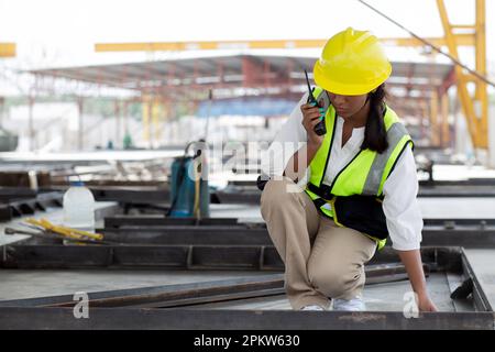 Young woman engineer using radio command with worker in construction site, architect or contractor speak to radio for control and planning development Stock Photo