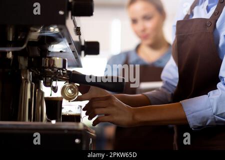 Closeup hands of barista preparing making coffee cappuccino or latte while pouring milk in coffee cup in cafe, close-up young asian woman making bever Stock Photo