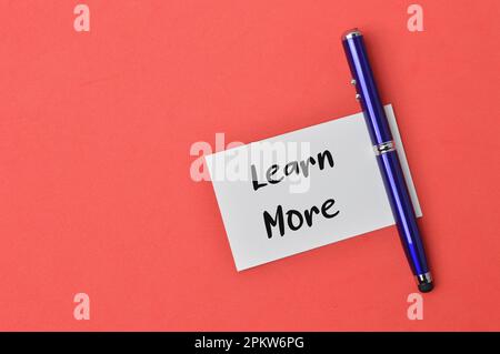 Pen and memo note written with text LEARN MORE over red background. Stock Photo