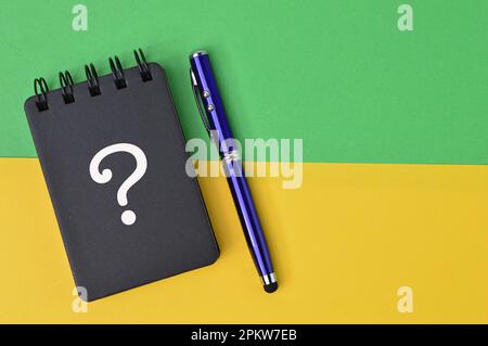 Question mark drawn on notebook over green and yellow background. Stock Photo