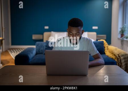 Young focused African American man freelancer working on laptop until late hours at home Stock Photo