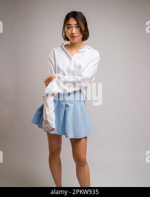 3/4 Body Portrait of Young Asian Woman Wearing a Short Blue Skirt and White Long Sleeve Shirt | White Backdrop Stock Photo