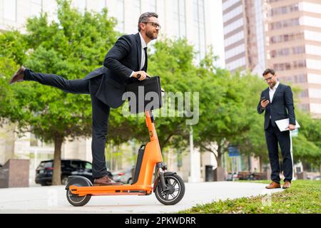 Funny business man in a suit riding an electric scooter on business meeting. Crazy businessman riding on scooter to work along the street in city Stock Photo