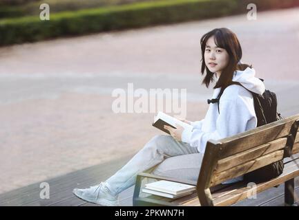 High school student and college student concept with backpack sitting on a park bench and reading and studying Stock Photo