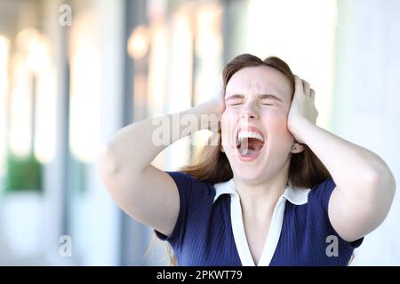 Stressed woman yelling standing in the street with hands on head Stock Photo
