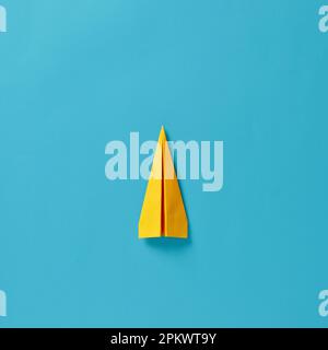 Yellow paper airplane on blue background. Top view. Stock Photo