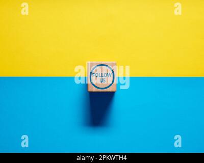 The word Follow Us on wooden cube button on blue and yellow background. Social media or internet followers concept. Stock Photo