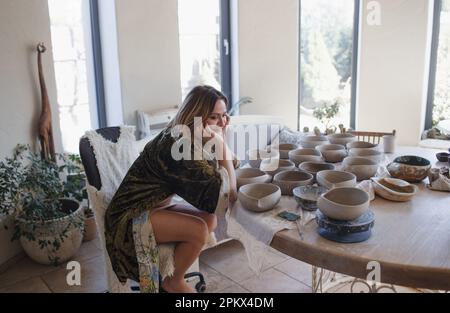 a woman is sitting at a large table in a ceramic studio. Stock Photo