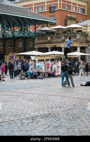 Street entertainer mounted on a tall unicycle puts on a show for a crowd of people in the Piazza, Covent Garden, London, England, UK Stock Photo
