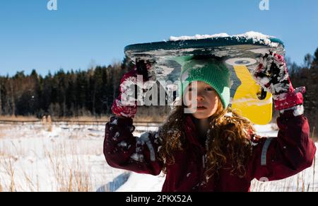 girl stood with her sledge in a sunny field of snow Stock Photo