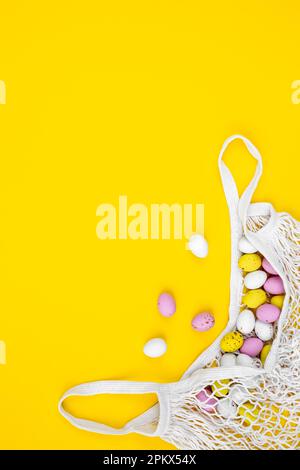 Colored Easter eggs in a mesh bag on a yellow background, flat lay. Stock Photo