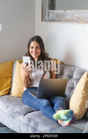 Woman Using A Laptop and Smartphone On Her Sofa Stock Photo