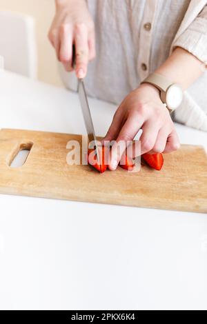 female cook cuts red fresh strawberries with knife in kitchen Stock Photo