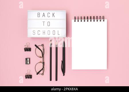 Back to school. Lightbox with letters and black colored stationery on a pink background. Empty notepad mockup. Stock Photo