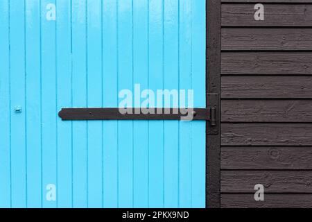 A two dimensional design created by a blue painted wooden door with a black hinge and dark wooden cladding Stock Photo