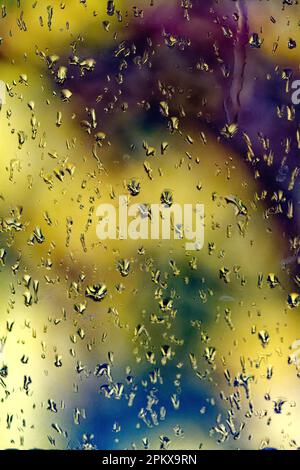 Close up of raindrops on window against a yellow and blue background Stock Photo