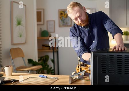 Professional worker repairing broken oven with tools in domestic kitchen Stock Photo